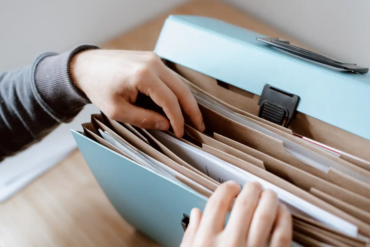 Hands sorting documents in an open accordion folder on a desk