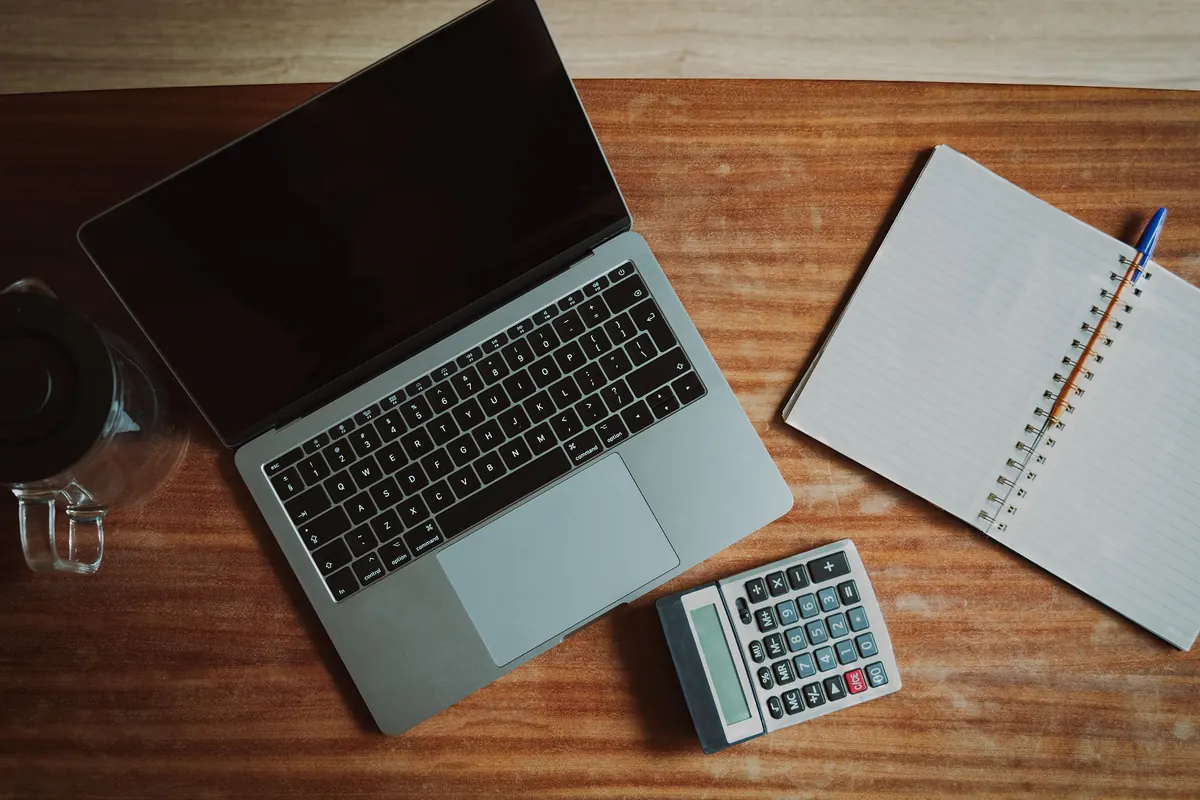 Laptop, calculator, and open notebook arranged on a desk