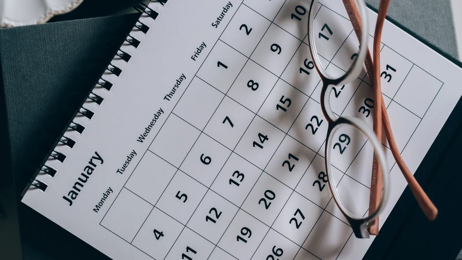 Eyeglasses resting on a monthly paper calendar
