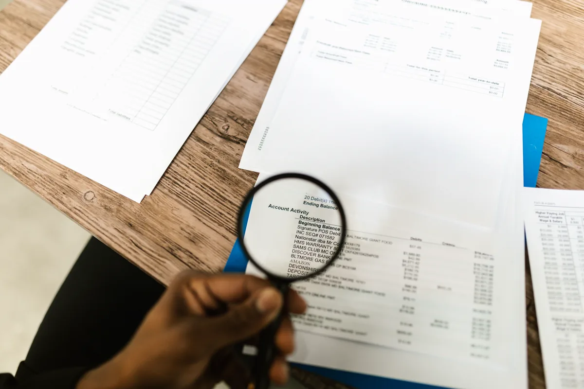 Person using a magnifying glass to review account activity on financial statements