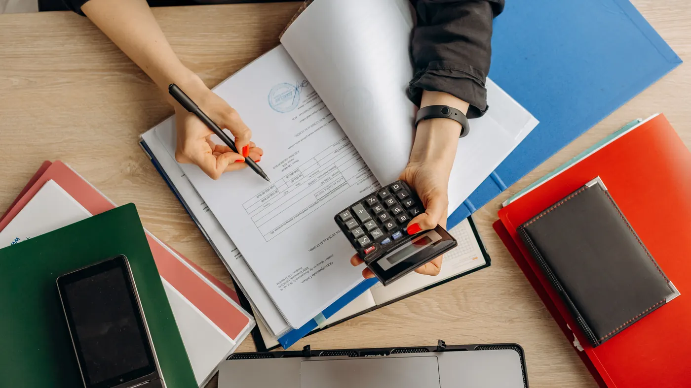 Hands using a calculator with financial records and organized folders