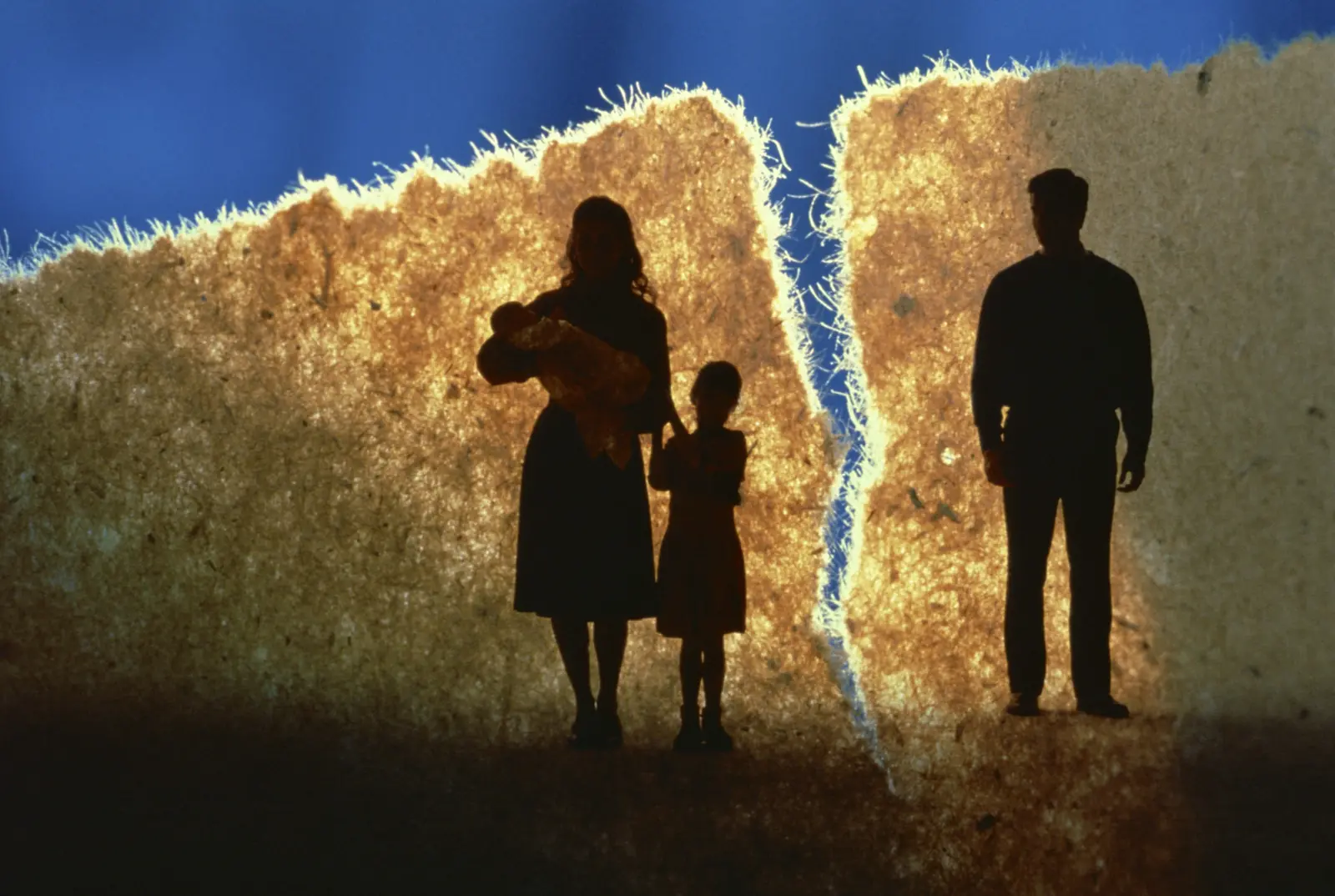 Silhouette of a mother and two children separated from a father by a tear in the background